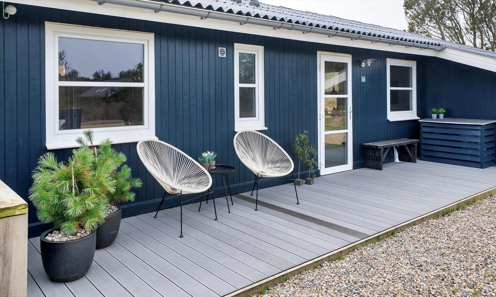 Terrasse mit zwei weißen Sesseln, Pflanzen und einer Tür.