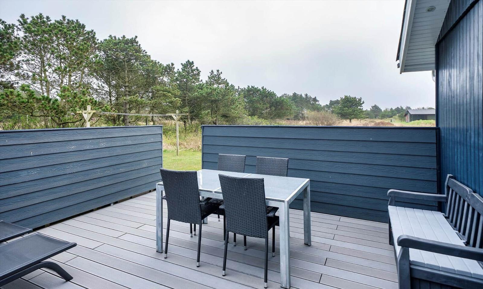 Terrasse mit Tisch, Stühlen und Liegestühlen. Blick auf Wald und Grasland.
