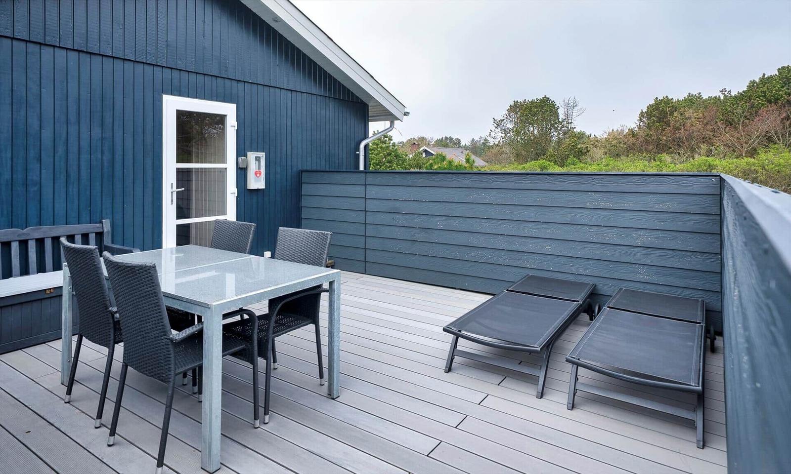 Terrasse mit Tisch, Stühlen und Liegen. Dunkelblaue Wand und Holzdielen.