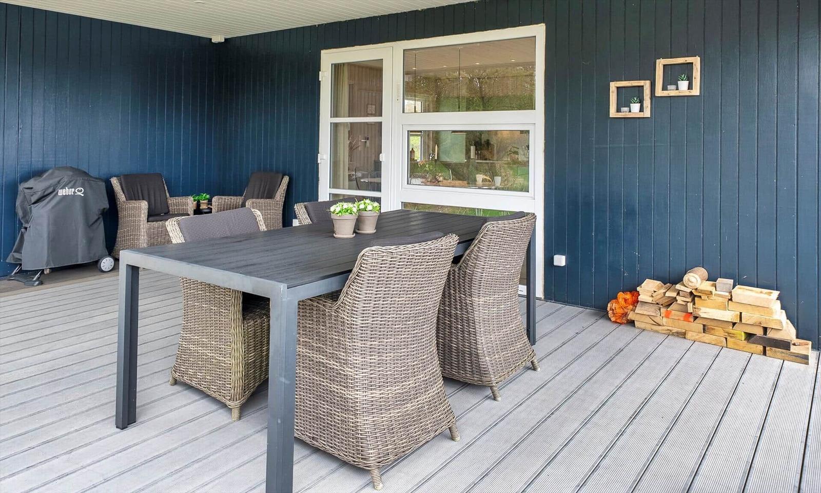 Terrasse mit Tisch, Stühlen, Grill und Holzstapel.
