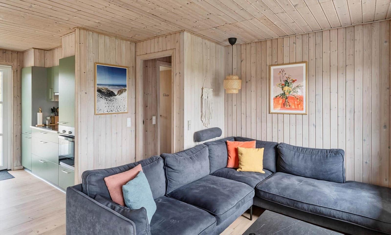 Wohnzimmer mit Ecksofa, Küchenbereich und Holzwandverkleidung.