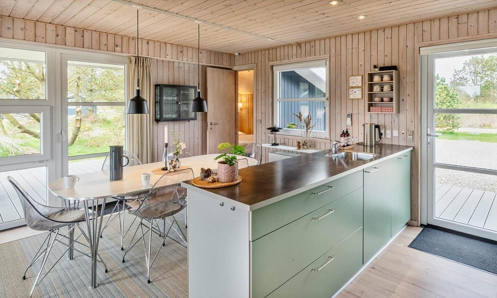 Küche mit Essbereich, Holzwand und Fenster zur Außenterrasse.