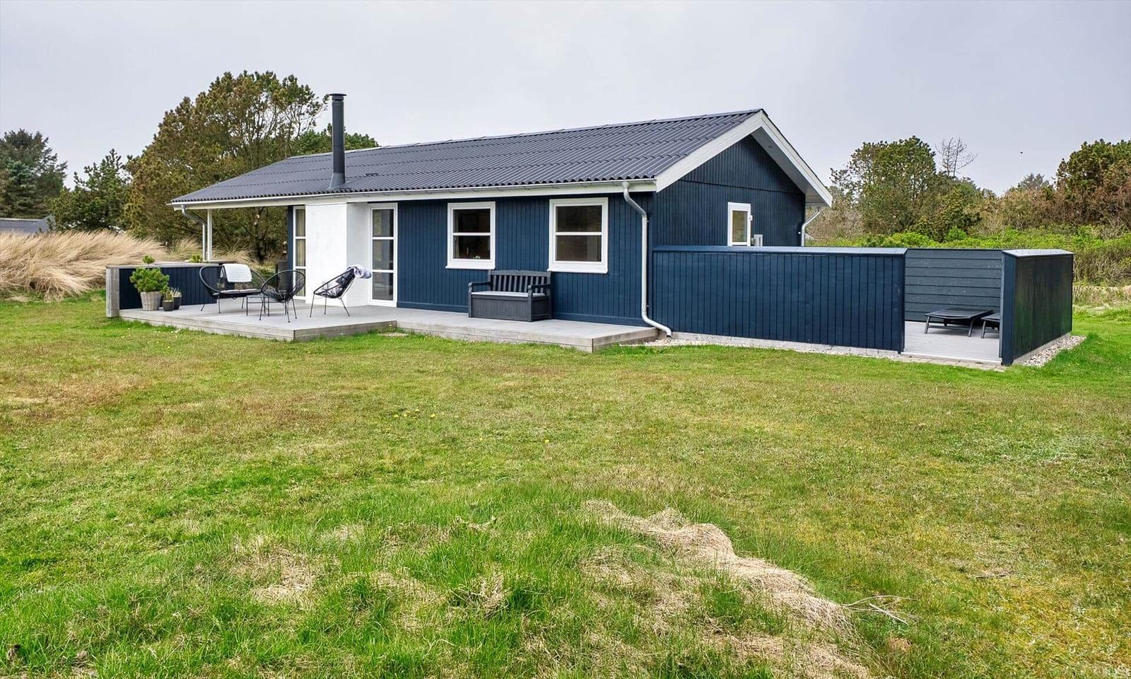 Ein blaues Haus mit Terrasse und Garten. Gartenmöbel und Sitzgelegenheit sind vorhanden.