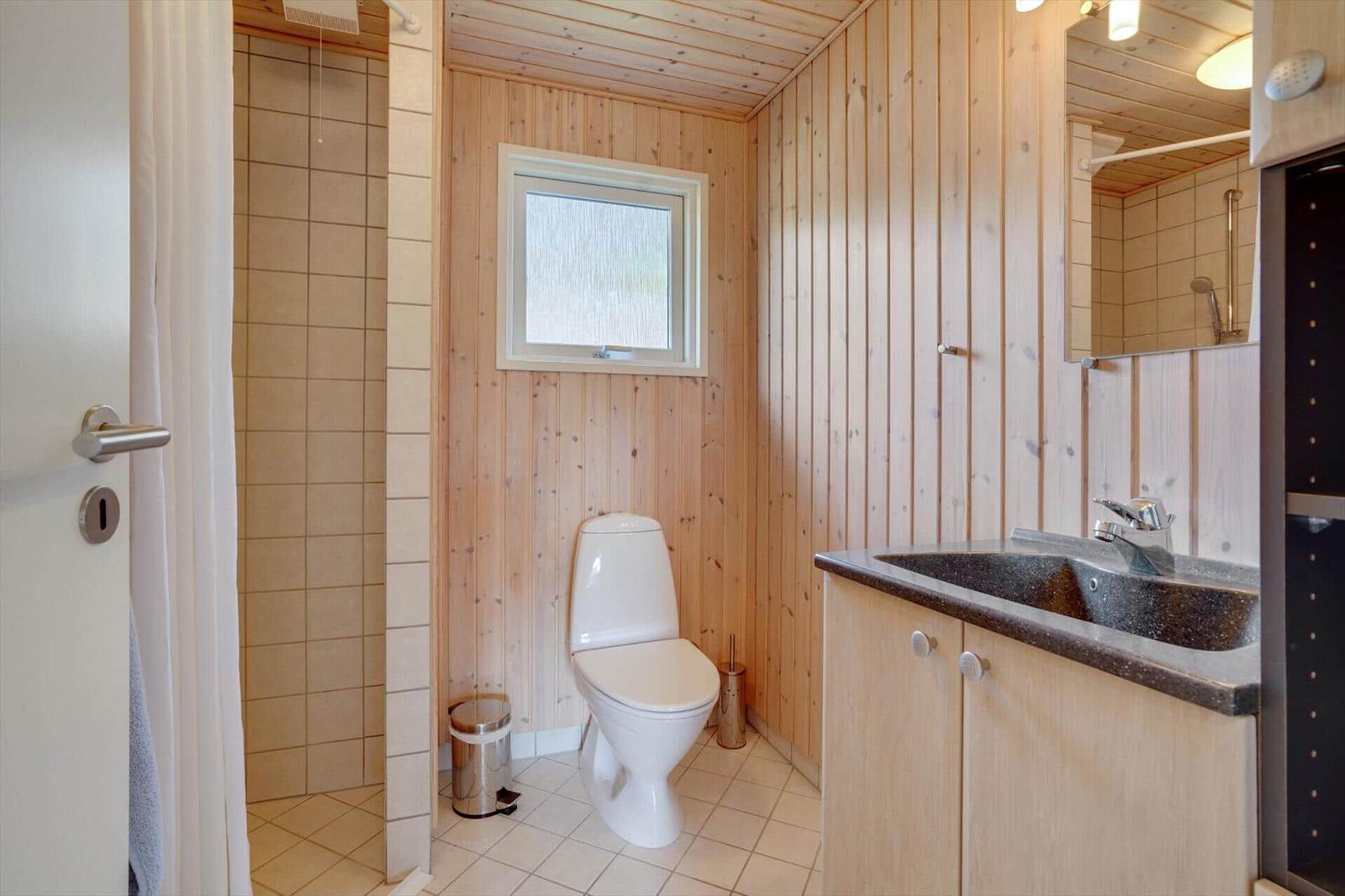 Badezimmer mit Toilette, Waschbecken und Dusche. Holzwände und Fliesenboden.