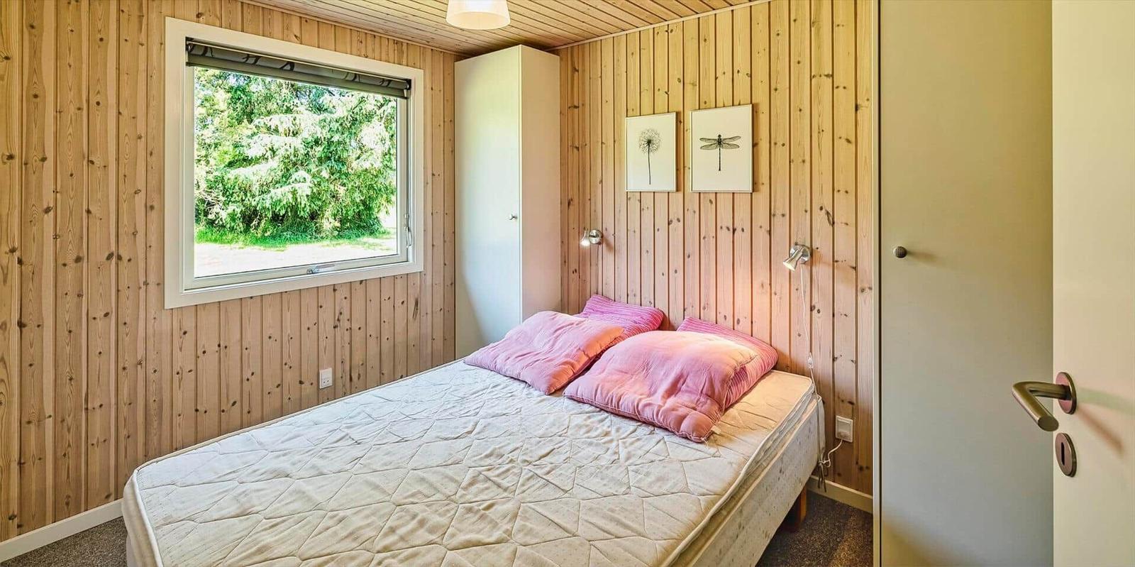 Schlafzimmer mit Holzwand, Bett und Fenster zum Grün.