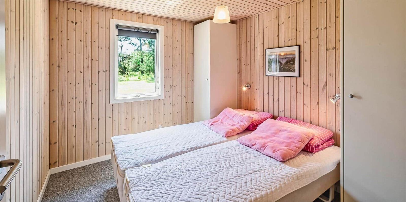 Schlafzimmer mit Holzwand, Bett und Fenster zum Garten.
