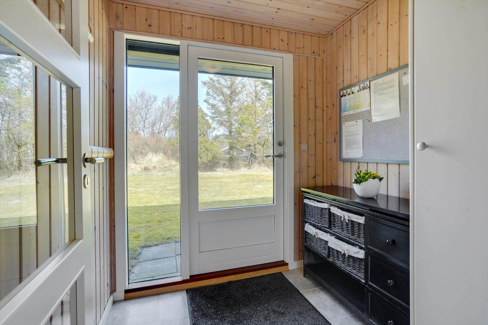 Eingangsbereich mit Glasfront, Holzwand und schwarzer Kommode mit Körben.