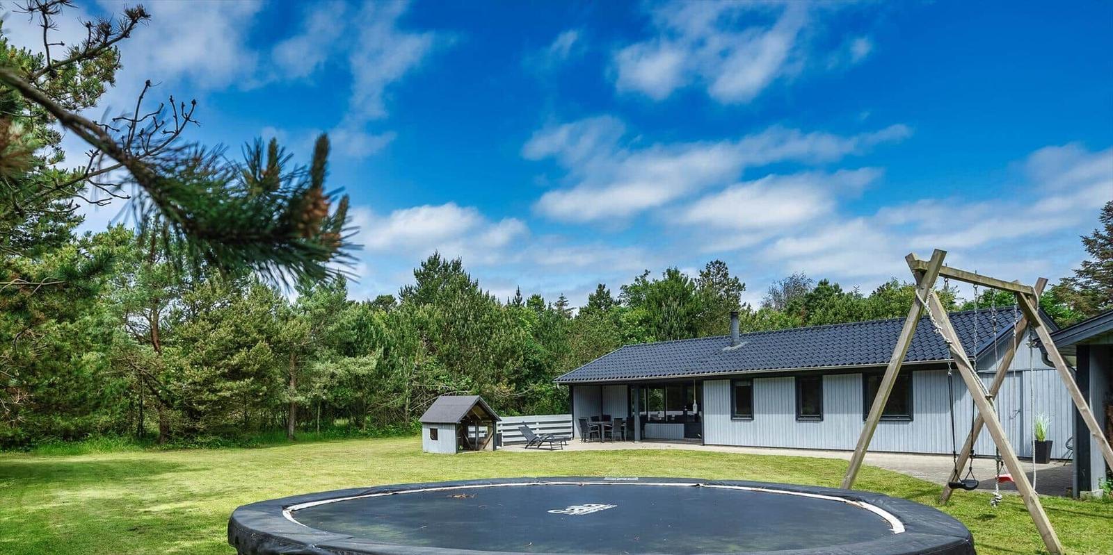 Haus mit Garten, Trampolin und Schaukel unter blauem Himmel.