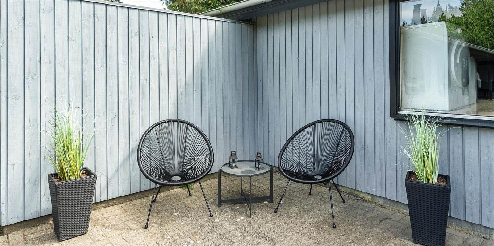 Terrasse mit zwei schwarzen Sesseln, Tisch und Pflanzen an grauer Holzwand.