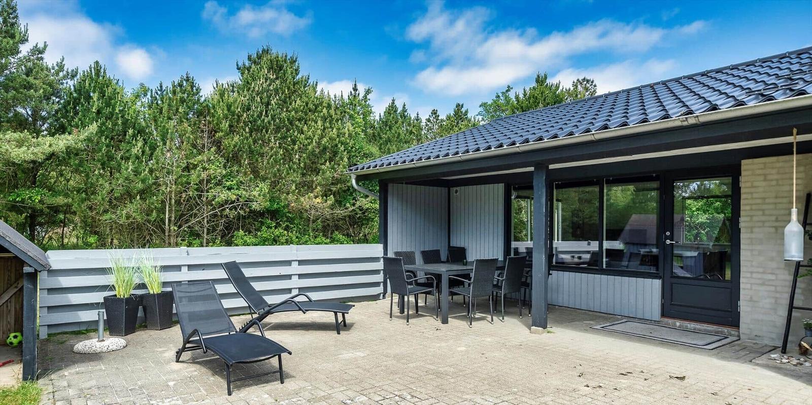 Terrasse mit Liegen und Tisch, angrenzend an modernes Haus mit Glasfront.