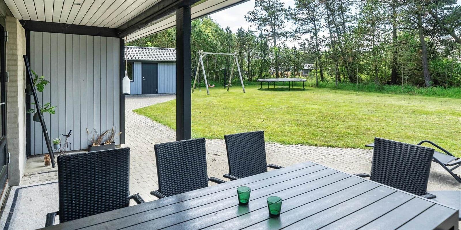 Terrasse mit Tisch und Stühlen, Blick auf grünen Garten mit Schaukel und Trampolin.