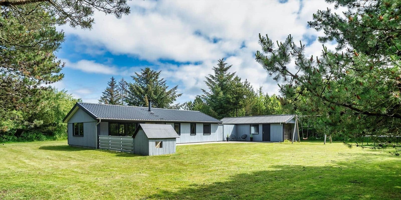 Ein graues Haus mit Dach und Garten. Umgeben von Bäumen und Gras.