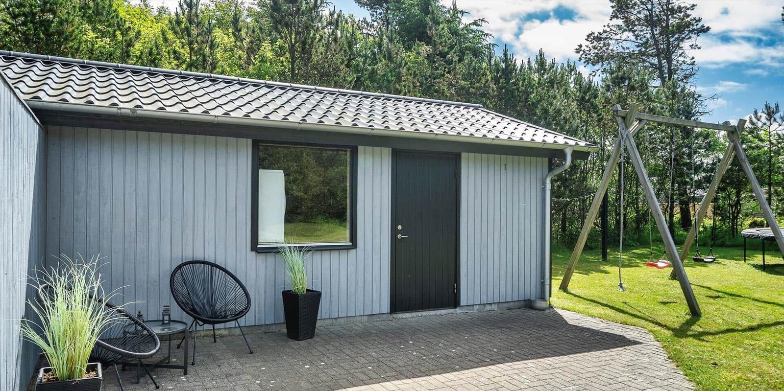 Moderne Hütte mit Terrasse, Schaukel und grünem Garten im Wald.