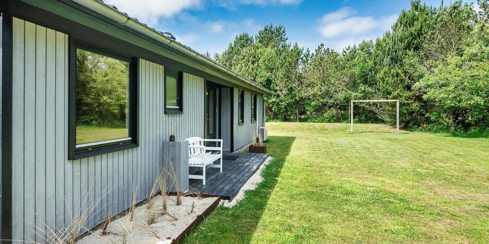 Moderne Hütte mit Terrasse, Garten und Fußballtor im Hintergrund.
