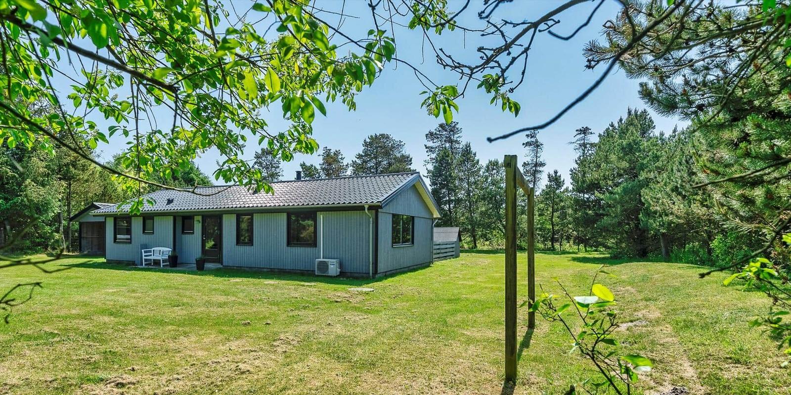 Ein kleines Haus mit grünem Garten und Bäumen im Hintergrund.