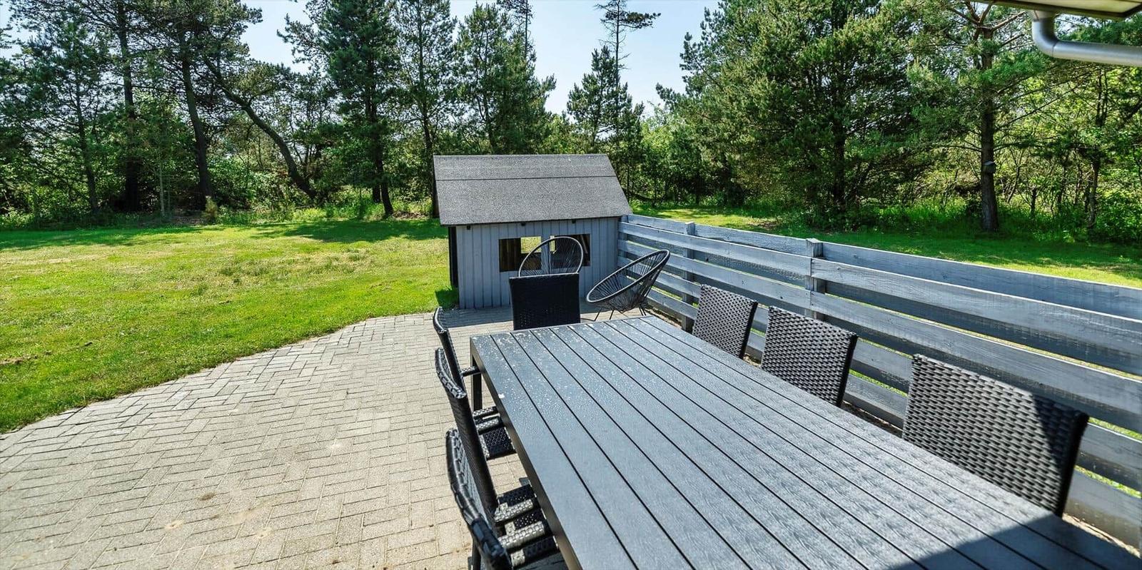Terrasse mit Tisch und Stühlen, kleiner Schuppen und grüner Rasen im Hintergrund.