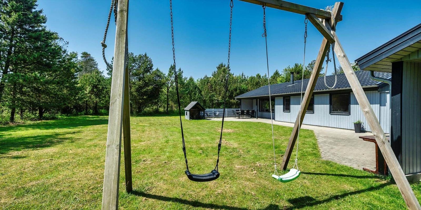Schaukeln im Garten vor einem Ferienhaus mit Wald im Hintergrund.