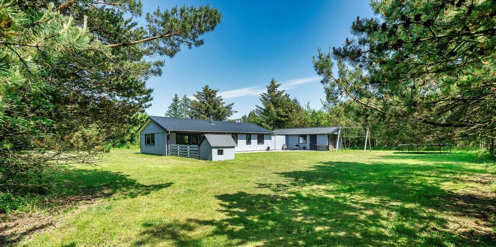Ein graues Haus mit Garten und umliegenden Bäumen unter blauem Himmel.