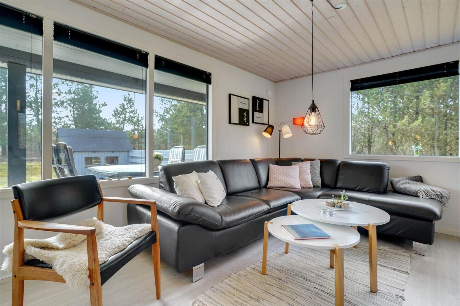 Wohnzimmer mit schwarzer Ledercouch, Holzstuhl und großen Fenstern.