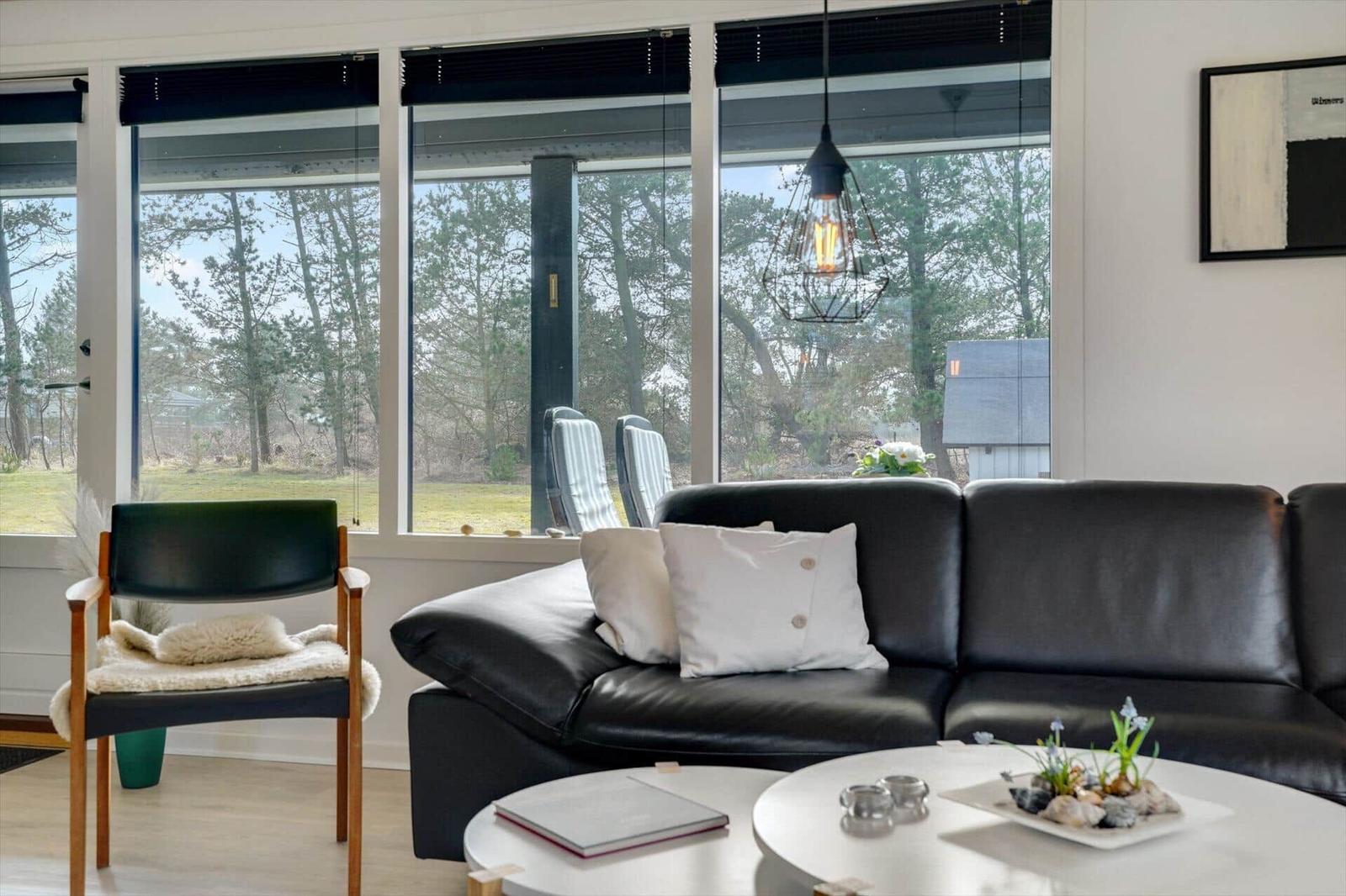 Wohnzimmer mit schwarzer Ledercouch, runden Tisch und Blick auf Wald.