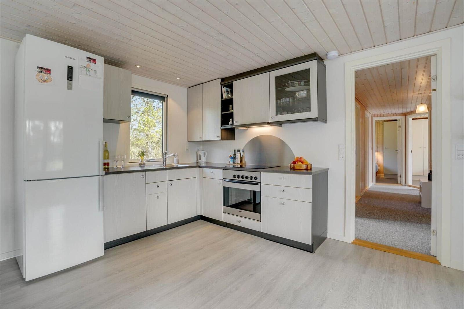 Küche mit Kühlschrank, Herd und Fenster. Durchgang zu Wohnbereich.