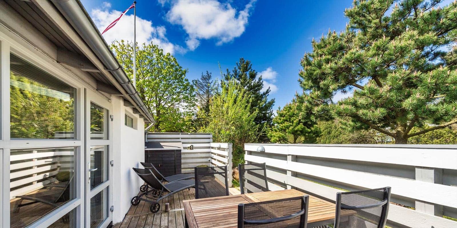 Terrasse mit Tisch, Stühlen und Liegestühlen. Hintergrund: Bäume und blauer Himmel.