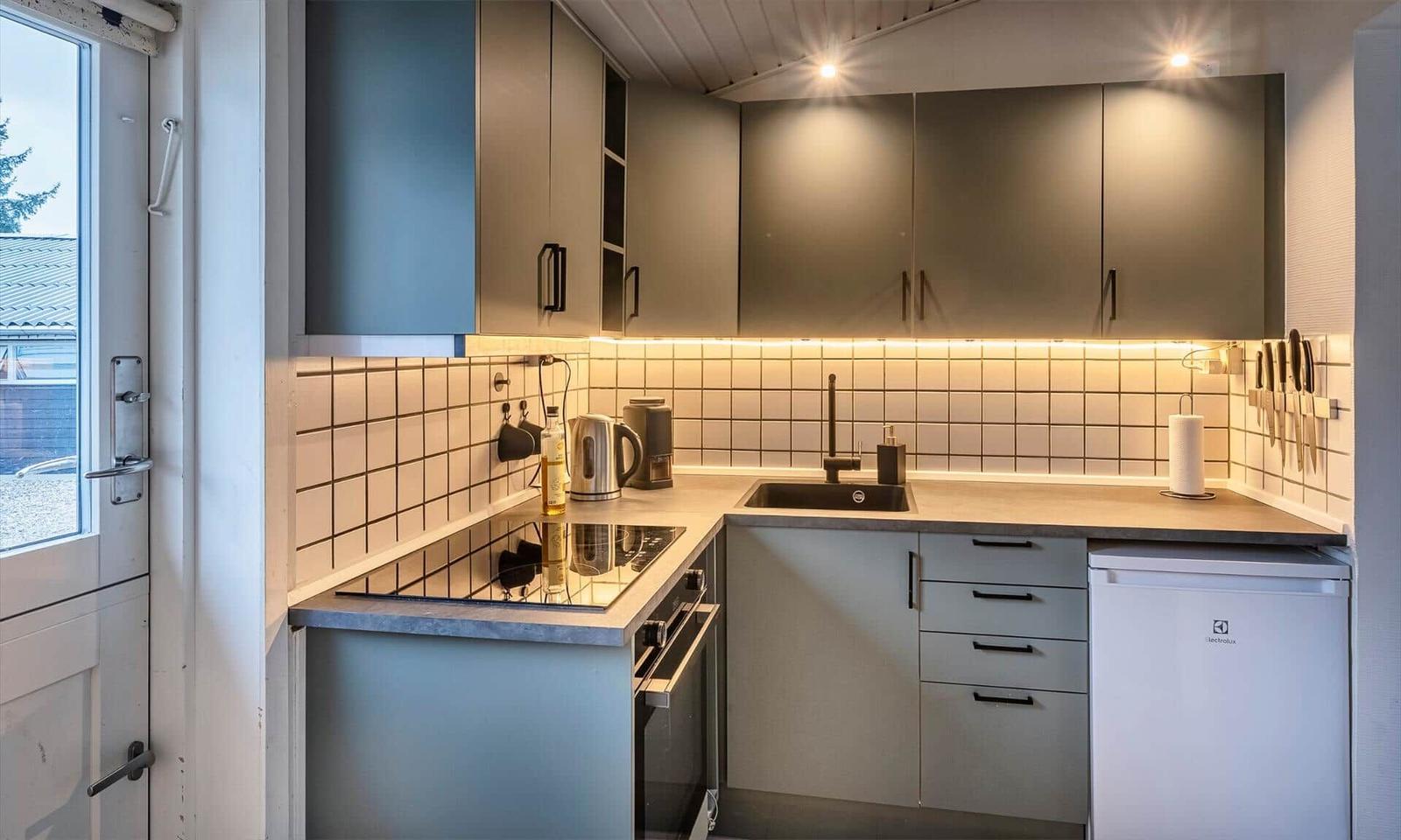 Küche mit Arbeitsplatte, Spüle und Kühlgerät. Hintergrund mit Fliesen und Licht.
