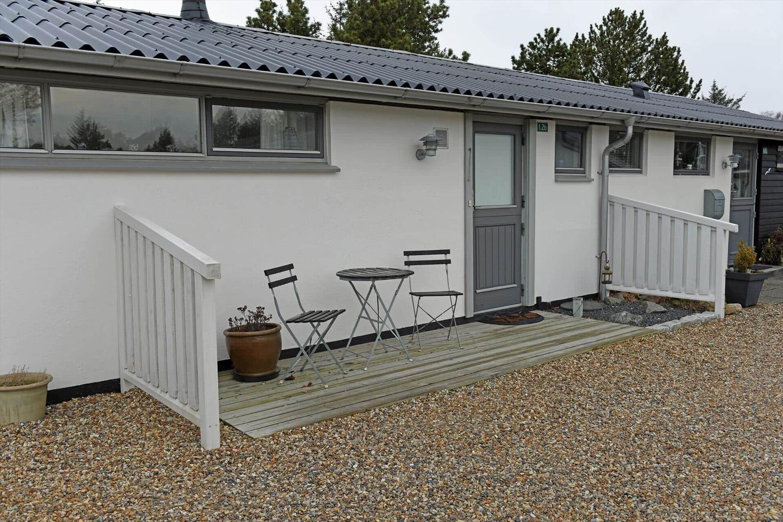 Wohnung mit Terrasse, Tisch und zwei Stühlen. Weiße Fassade, graue Tür und Dach.