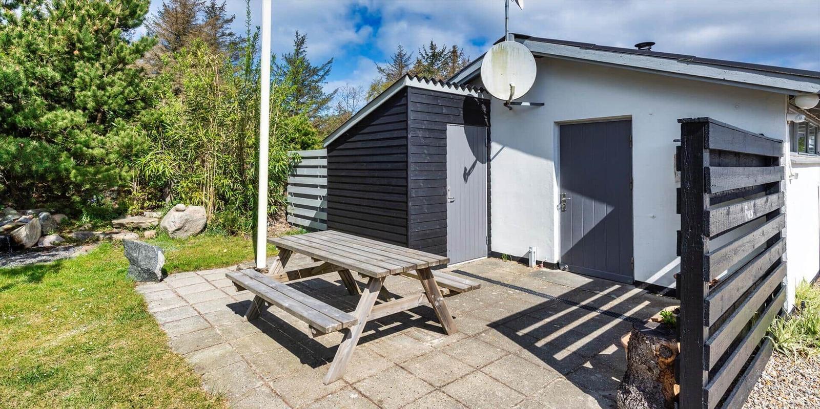 Außenbereich mit Picknicktisch, Garten und Holzhaus neben weißer Wand.