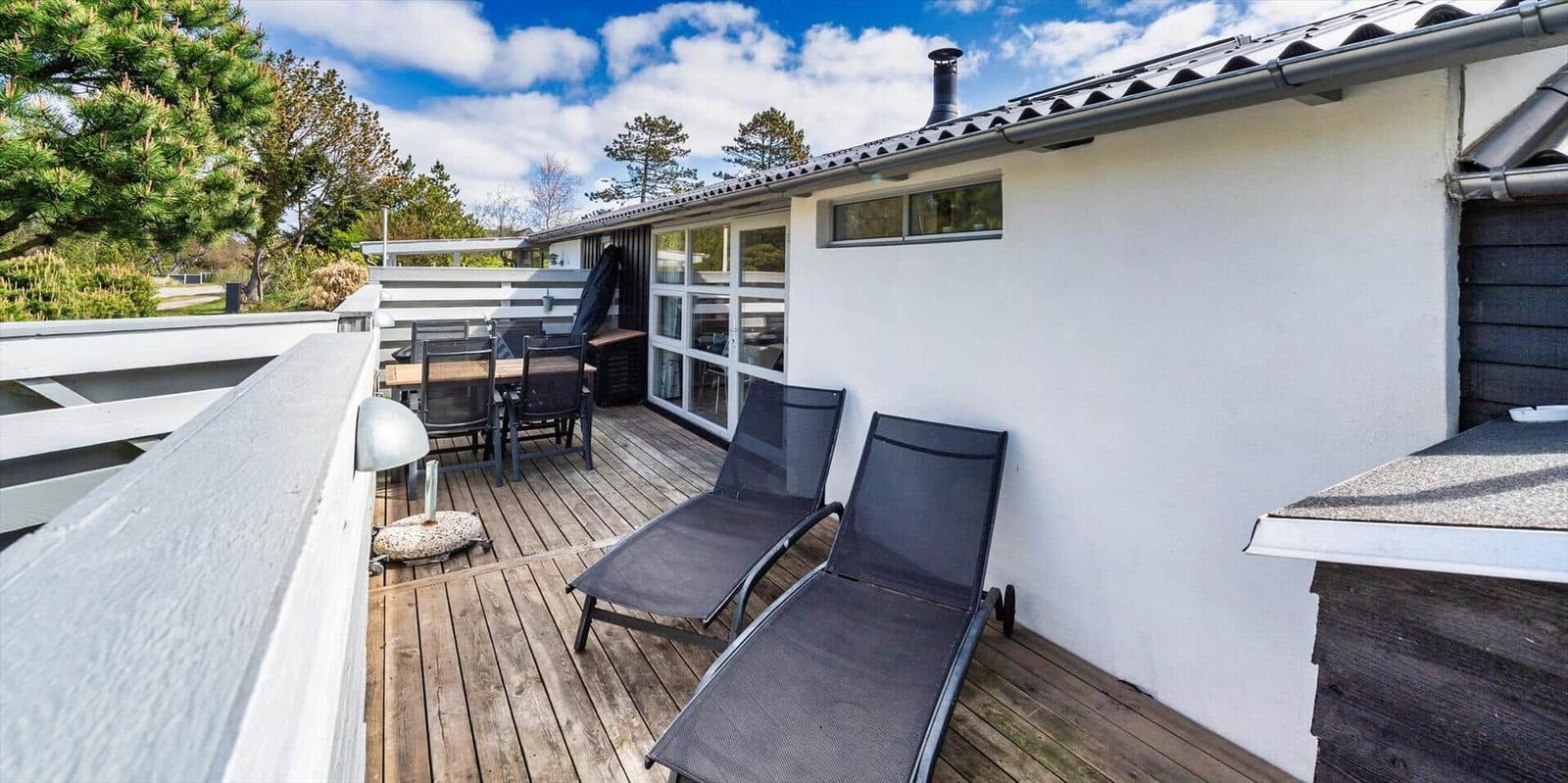 Terrasse mit Liegen und Tisch, Blick auf Bäume und Himmel.