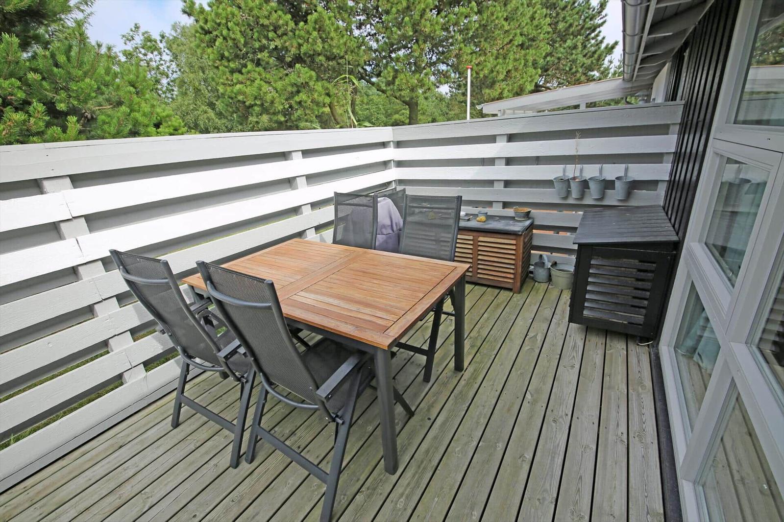 Terrasse mit Holztisch, Stühlen und Grillplatz. Umzäunt mit weißem Holzgeländer.