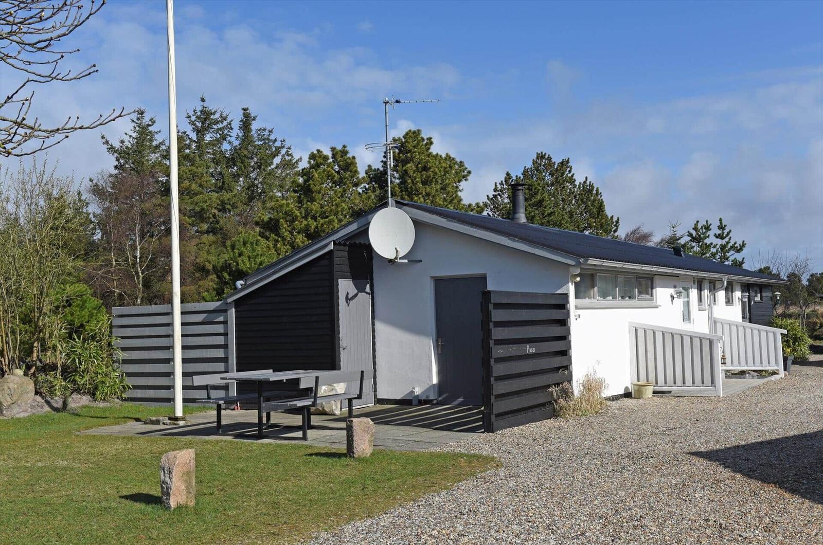 Ein Haus mit Grillplatz, Satellitenschüssel und Holzverkleidung. Gras, Kies und Bäume umgeben es.