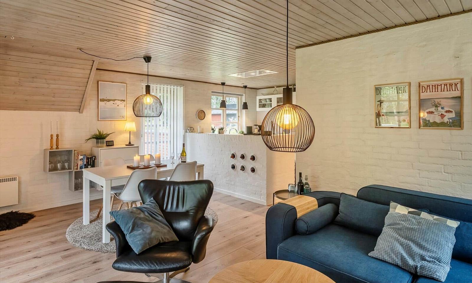 Wohn- und Essbereich mit Sofa, Sessel und Tisch. Decke aus Holz, weiße Wände und Beleuchtung.