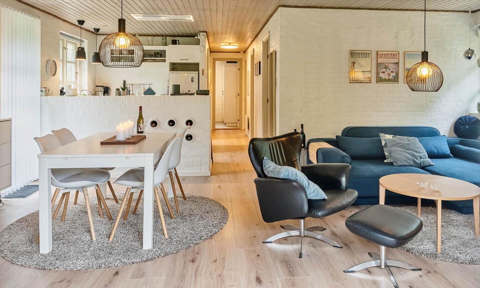Wohn- und Essbereich mit blauem Sofa, schwarzer Ledersessel und Holzboden.