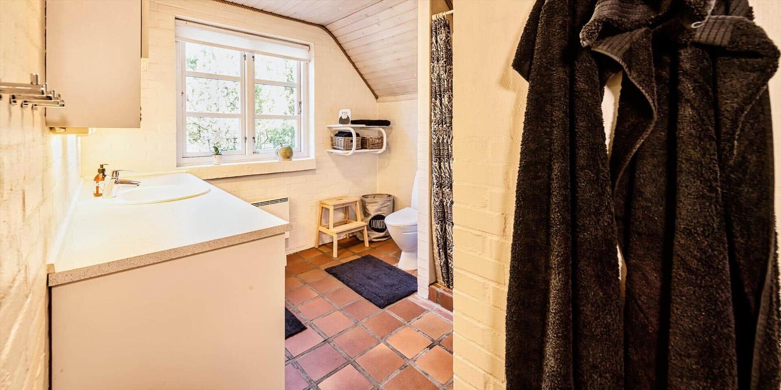 Badezimmer mit Waschbecken, Toilette und Dusche. Terrakottafußboden und Fenster mit Blick.