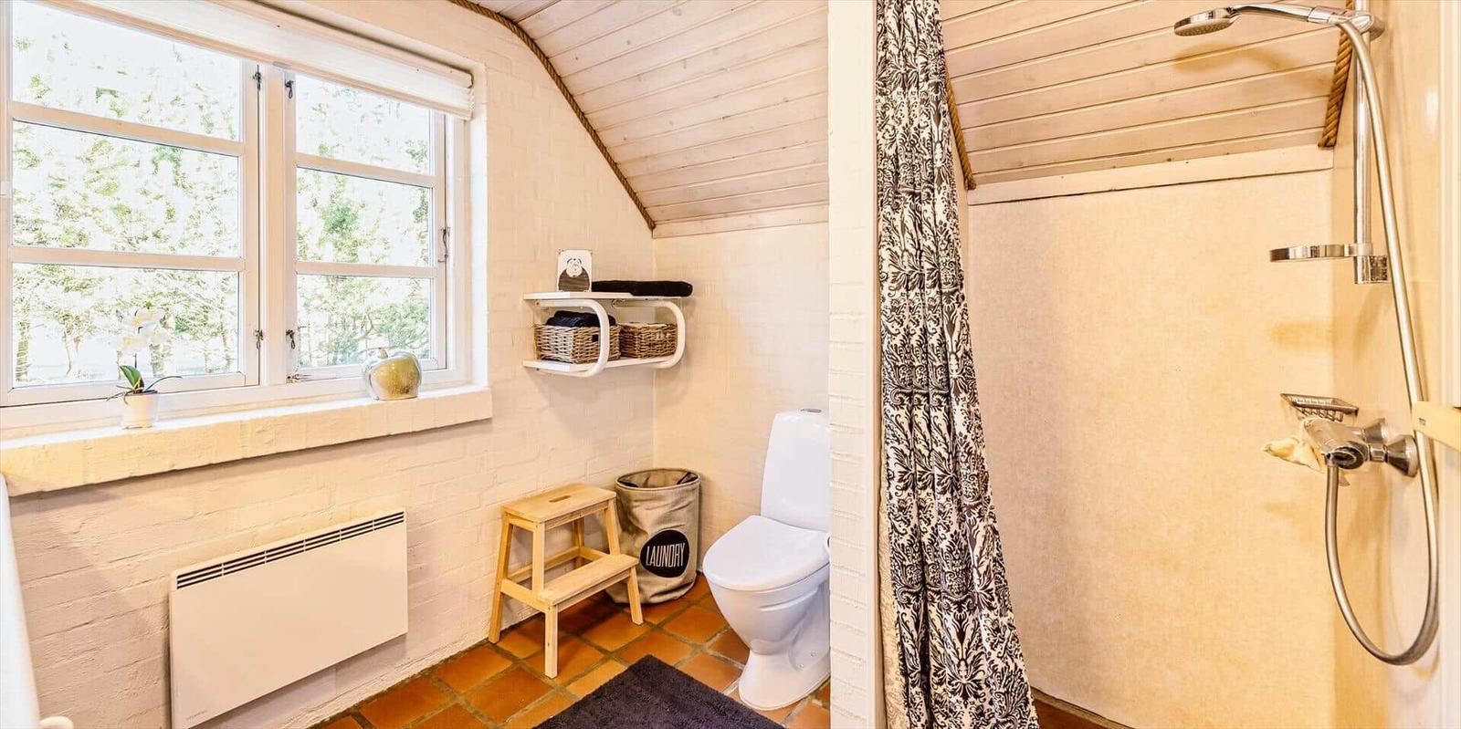 Badezimmer mit Dusche, Toilette und Fenster mit Blick auf Grün.