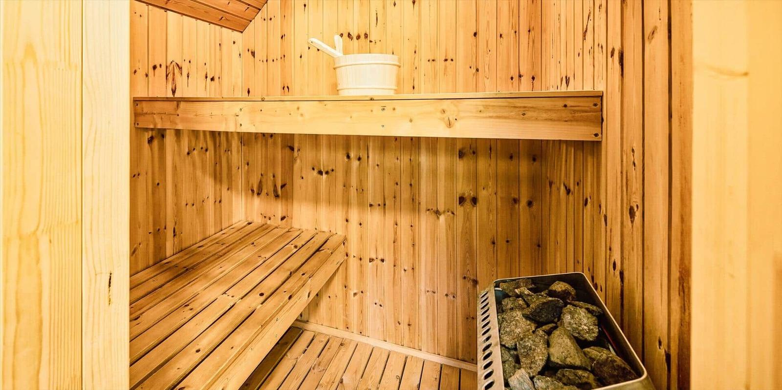 Holzsauna mit Sitzbank, Steinmulde und Wassereimer.