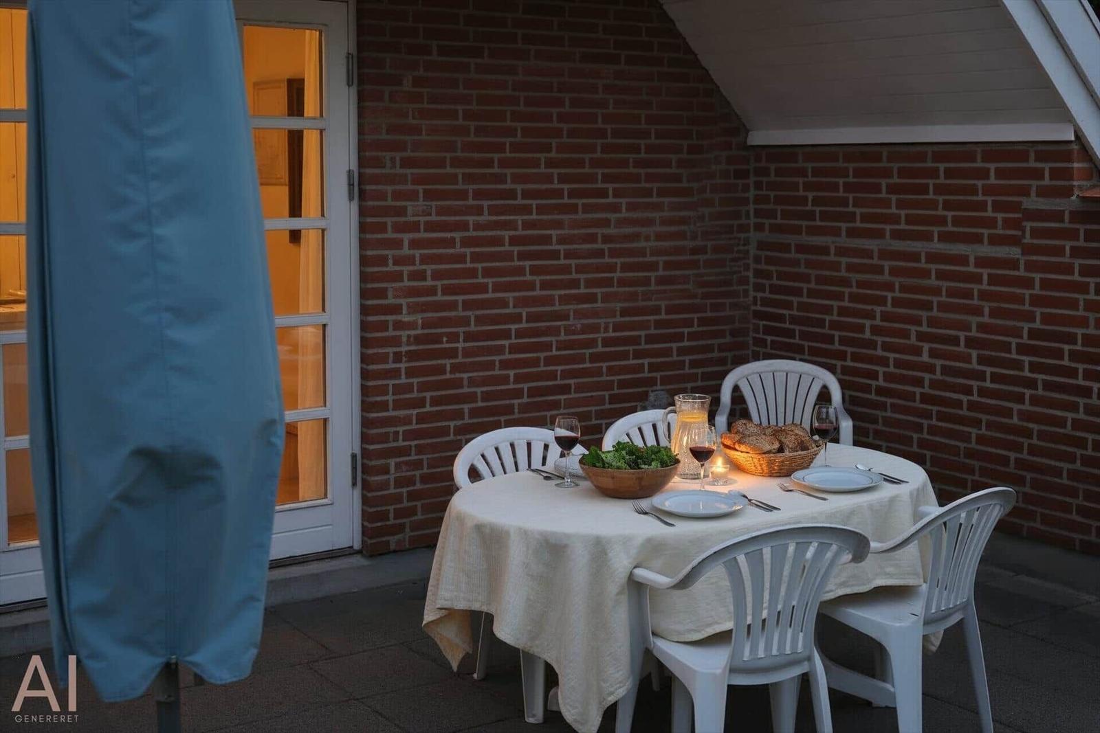 Rundtisch mit Tischdecke, Tellern und Stühlen auf Terrasse mit Backsteinwand.