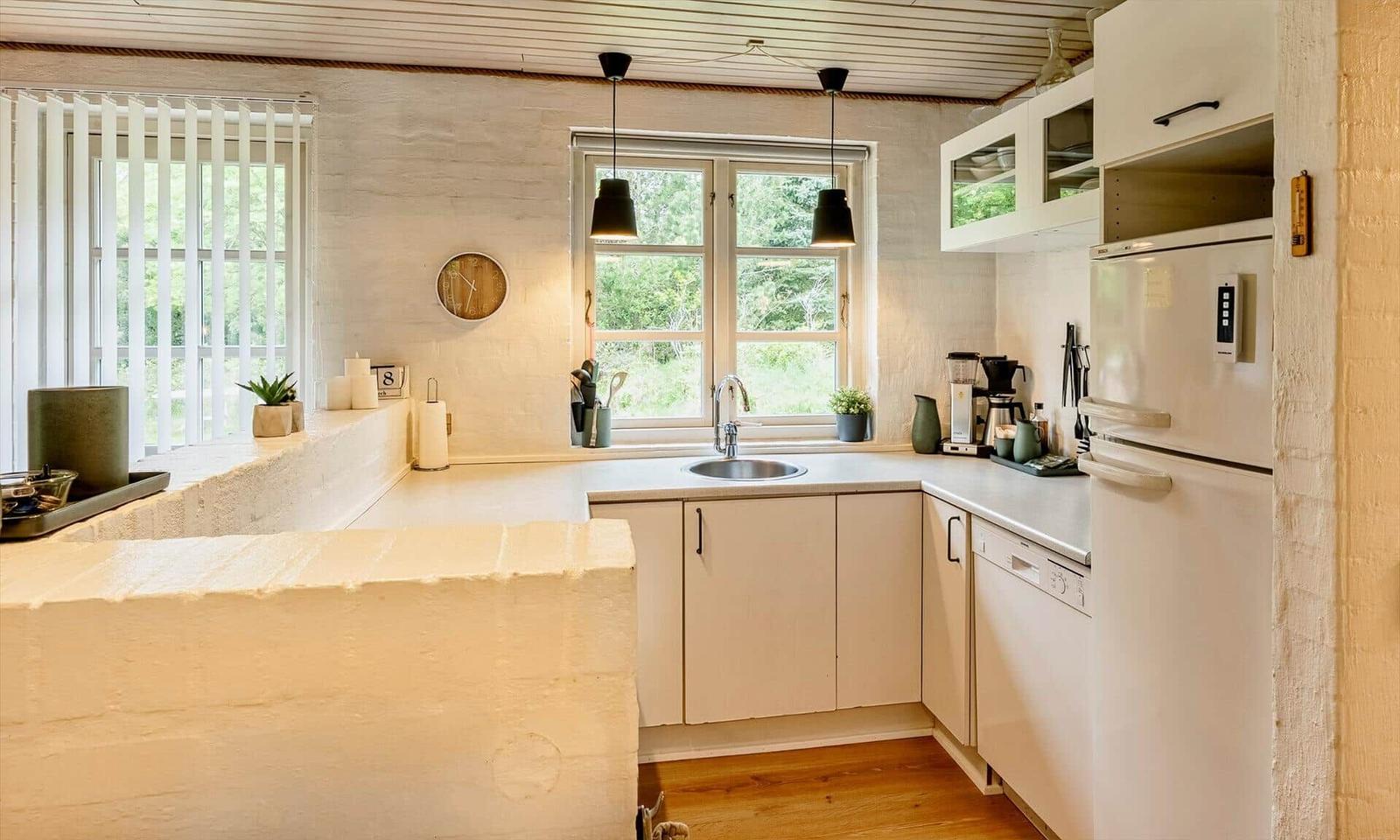 Küche mit Arbeitsfläche, Spüle, Kühlschrank und Fenster mit Blick auf Grün.
