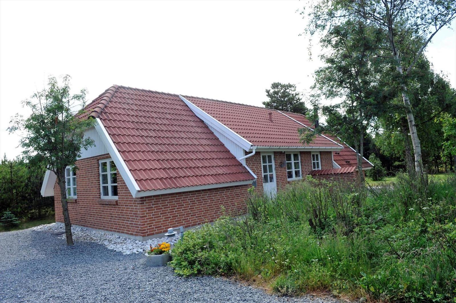 Ein Haus mit rotem Dach und Backsteinfassade umgeben von Grünflächen und Bäumen.