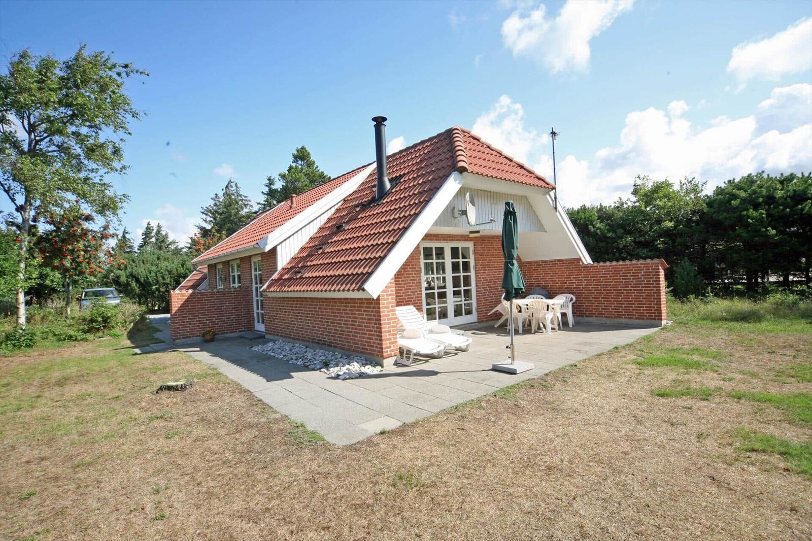 Haus mit Terrasse, Liegen und Tisch. Umgeben von Grün und Bäumen.