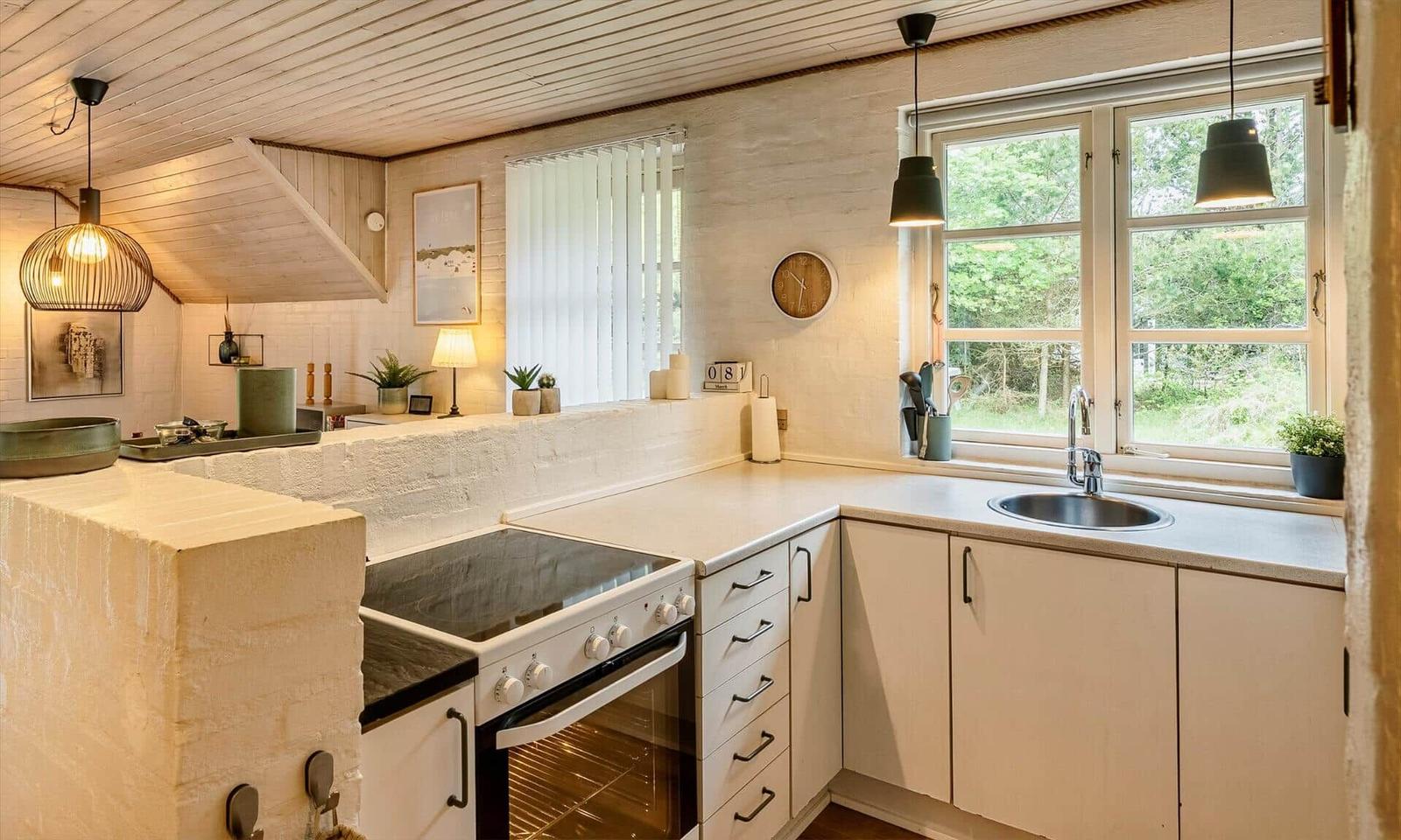Küche mit weißen Schränken, Arbeitsplatte und Fenster. Holzdecke und Pendelleuchten.