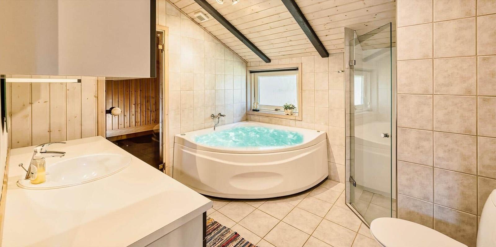 Badezimmer mit Whirlpool, Dusche und Waschbecken. Holzdecke und Fliesenwand.