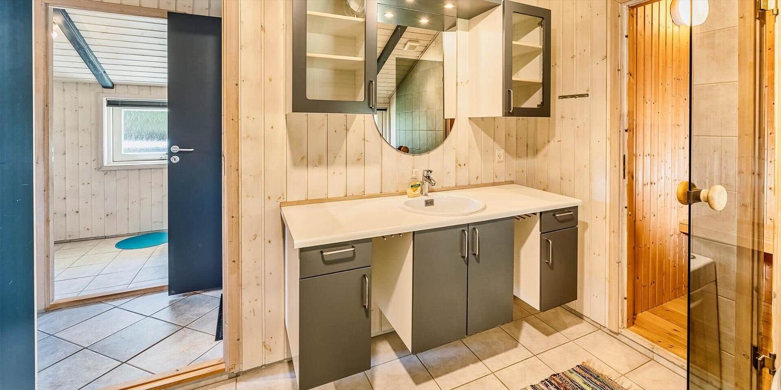 Badezimmer mit Waschbecken, Spiegelschrank und Dusche. Holzwände und Fliesenboden.
