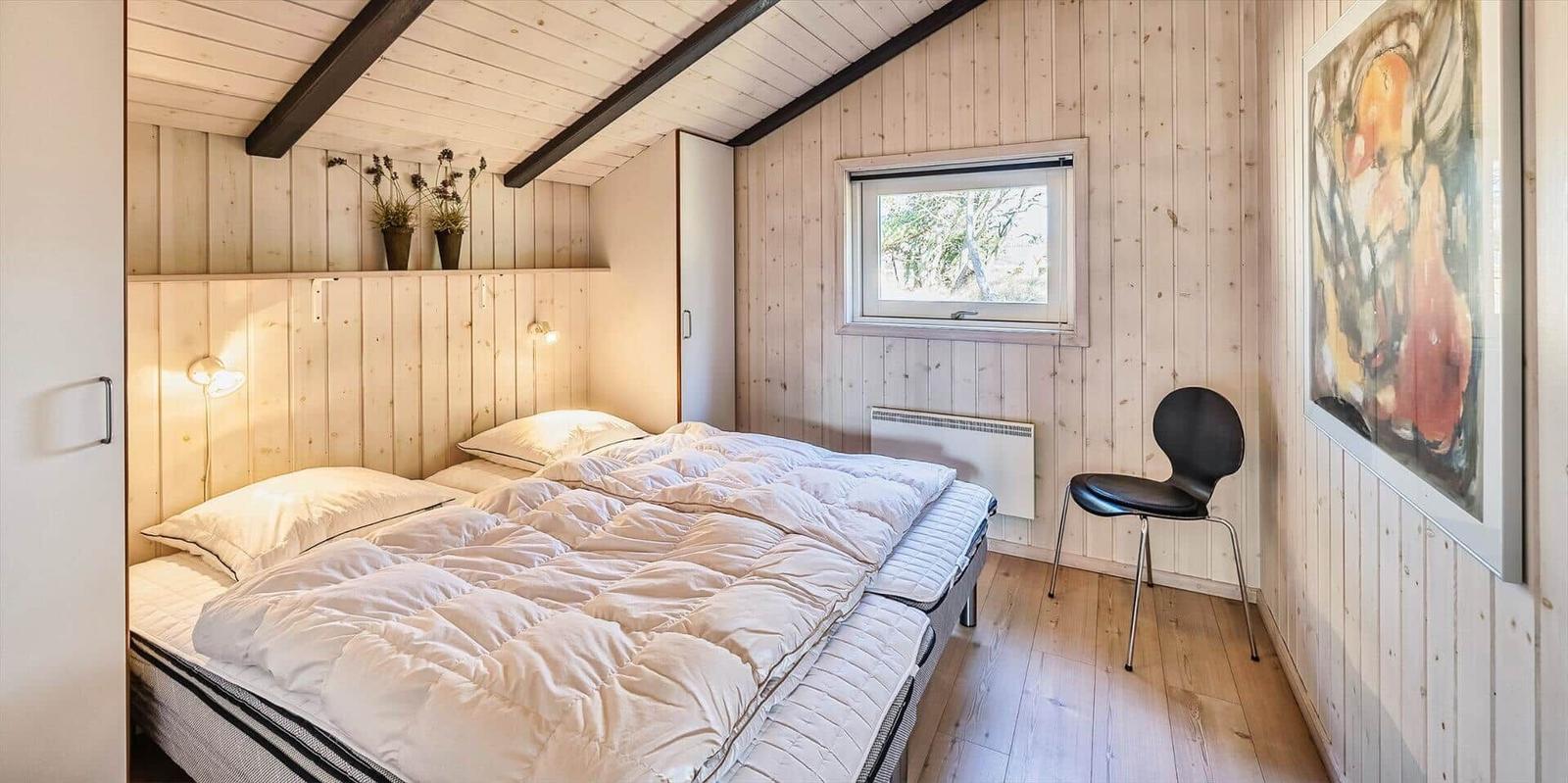 Schlafzimmer mit Holzwand, Bett, Stuhl und Fenster