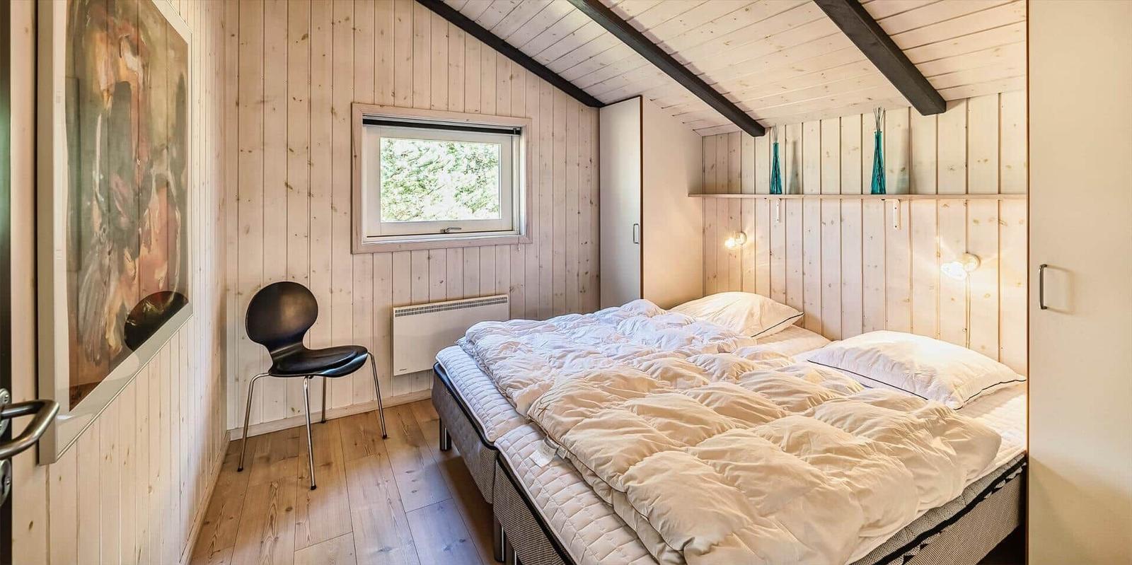 Schlafzimmer mit Bett, Stuhl und Fenster. Holzwände und Dachschräge.