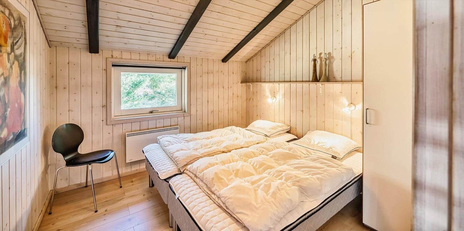 Schlafzimmer mit Doppelbett, Fenster und Holzwandverkleidung.