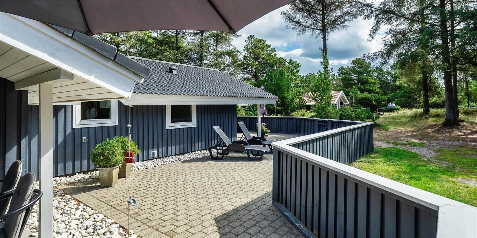 Terrasse mit Liegestühlen und Sonnenschirm neben einem blauen Holzhaus.