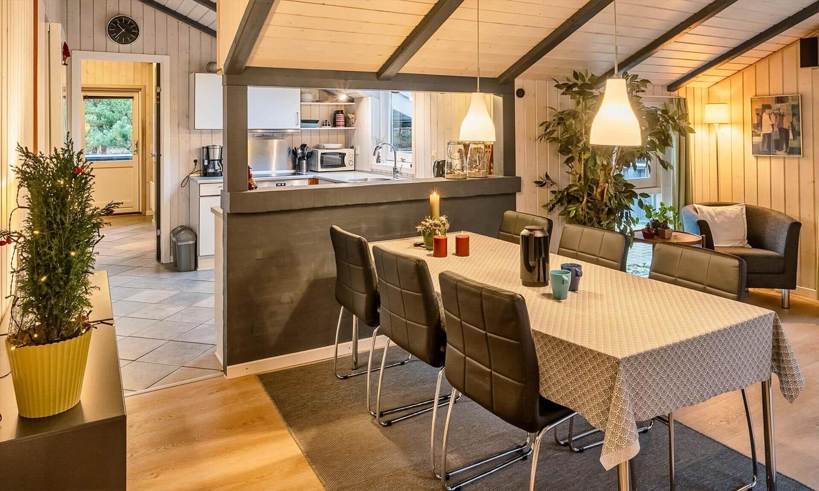Essbereich mit Tisch und Stühlen, Küchenbereich im Hintergrund, Holzwände und Pflanzen.
