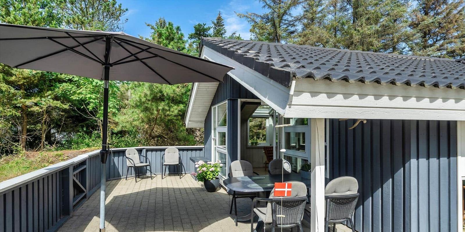 Terrasse mit Sonnenschirm, Tisch und Stühlen vor einem Haus mit blauem Holzverkleidung.